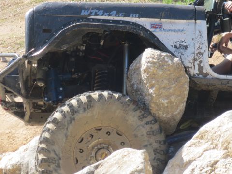1989 Ford Bronco - This modified off-road vehicle is navigating a rocky terrain, with its large tire pressed against a boulder.