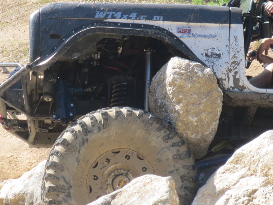 Off-road vehicle tire wedged against a large rock, showing suspension and fender detail. Text 'WT4x4.com' visible