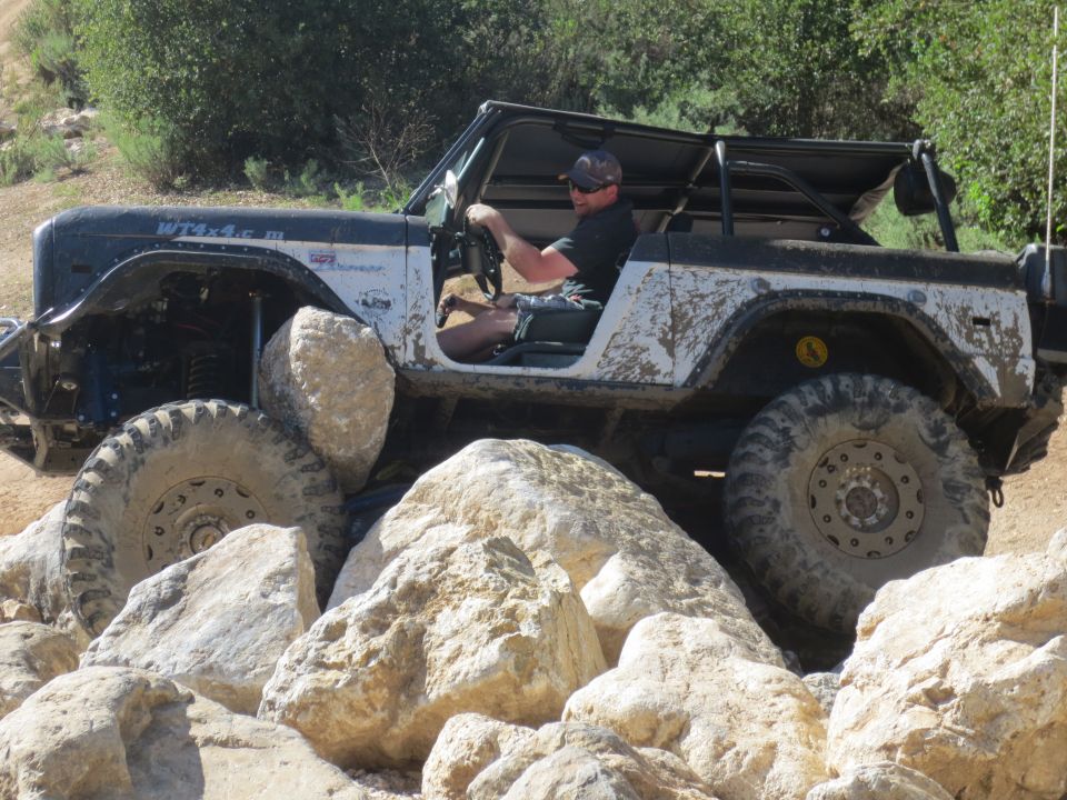 Man driving a lifted, mud-splattered 1978 Ford Bronco over large rocks on a trail