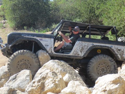1989 Ford Bronco - A man drives a heavily modified Ford Bronco through a rocky terrain.