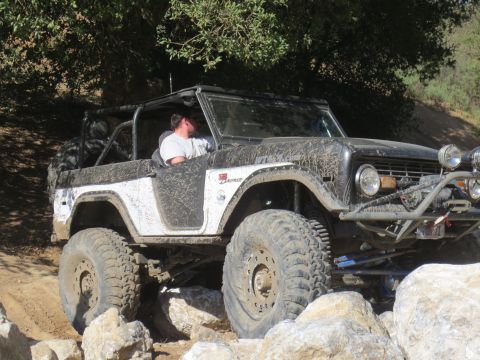1989 Ford Bronco - This heavily modified first-generation Ford Bronco is shown tackling a rocky trail, its body covered in mud from the off-road adventure.