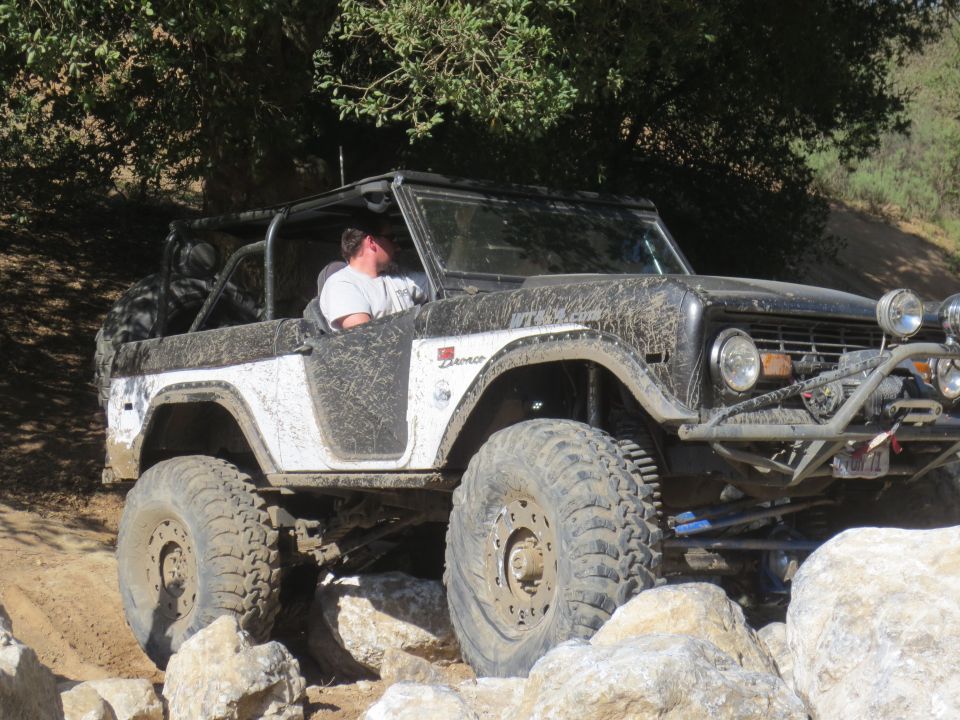 Mud-splattered first-generation Ford Bronco with off-road modifications navigating rocks