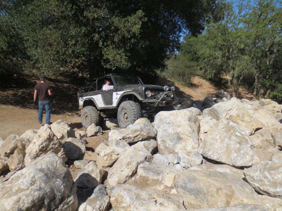 Modified Ford Bronco navigating a rocky trail, driver visible