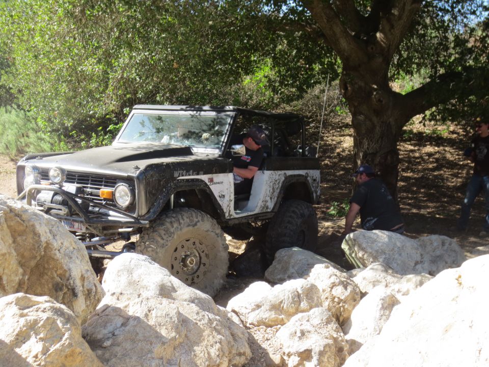 Black and white Ford Bronco off-roading over rocks, driver visible