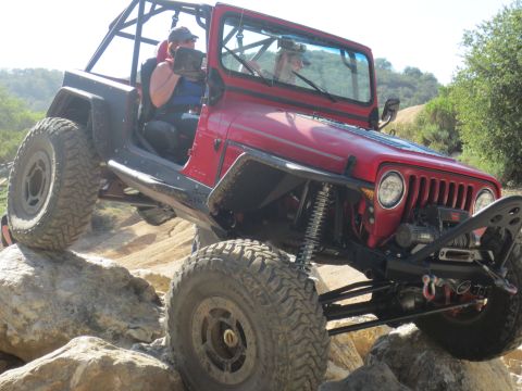 1989 Ford Bronco - A modified Jeep navigates a rocky off-road course with two people inside.