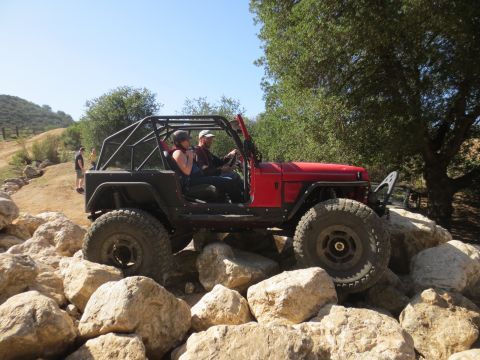 1989 Ford Bronco - Off-roading in a modified jeep over large rocks on a sunny day.