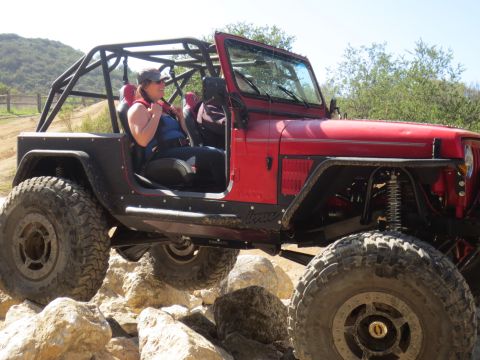 1989 Ford Bronco - A red Jeep Wrangler navigates a rocky terrain with a person inside.