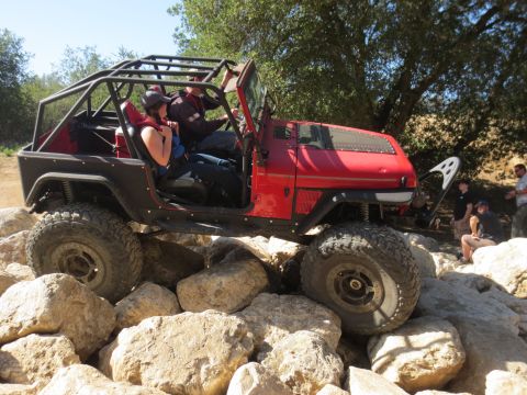 1989 Ford Bronco - Off-road Jeep Wrangler tackling a rocky obstacle with passengers inside.