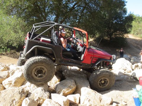 1989 Ford Bronco - A red off-road Jeep with a roll cage is shown traversing a rocky terrain.