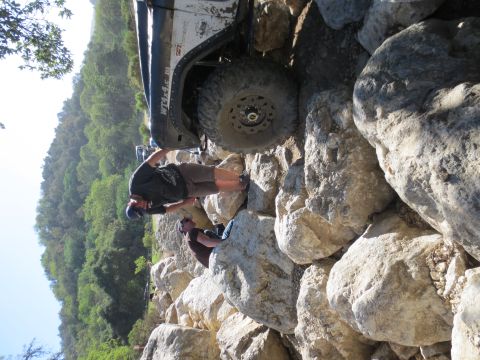 1989 Ford Bronco - A person checks the tire of an off-road vehicle as it maneuvers over large rocks on a steep incline.