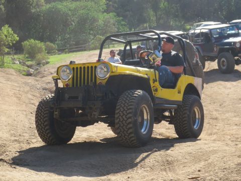 1989 Ford Bronco - A yellow Jeep navigates a dirt path with other off-road vehicles in the background.