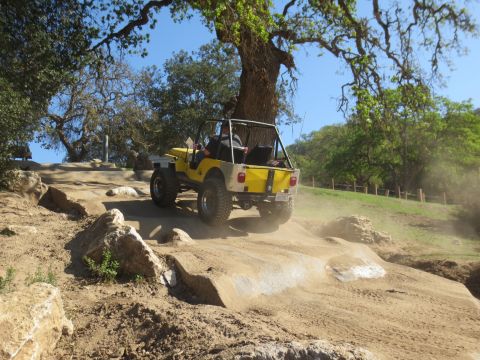 1989 Ford Bronco - Jeep navigating a challenging dirt trail with rocks and dust kicked up.