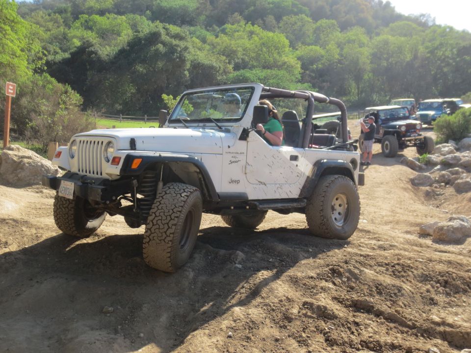 White Jeep Wrangler on a dirt trail, mud splattered on the doors and fenders