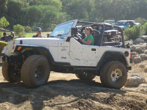 1989 Ford Bronco - A white Jeep Wrangler navigates an off-road trail with other vehicles visible in the background.