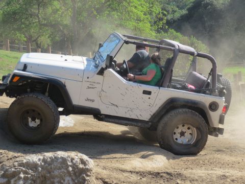 1989 Ford Bronco - A white Jeep Wrangler navigates a dusty off-road course with two occupants.