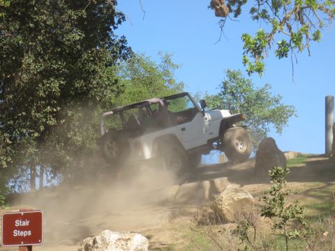 1989 Ford Bronco - A white Jeep Wrangler navigates a rocky trail, creating a cloud of dust.
