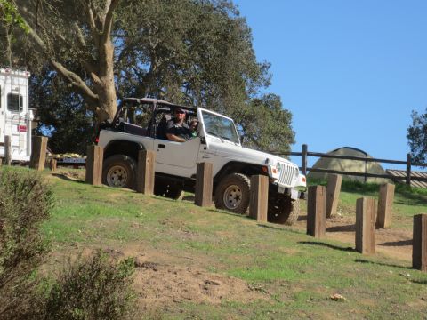 1989 Ford Bronco - A white Jeep Wrangler is parked on a grassy incline, with a trailer and RV visible behind it under a large tree.