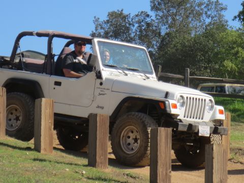 1989 Ford Bronco - A white Jeep Wrangler is driven on a dirt path, with two people inside.