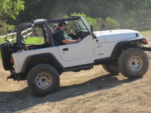 1989 Ford Bronco - A white Jeep Wrangler is driven by a man with a passenger on a dirt path.