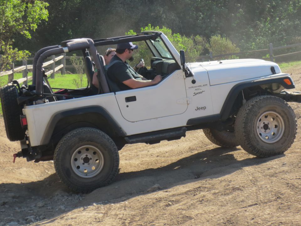 White Jeep Wrangler driving on a dirt road, with two people inside