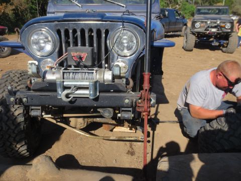 1989 Ford Bronco - A blue Jeep CJ-7 is worked on by a man, with another off-road vehicle visible behind it.