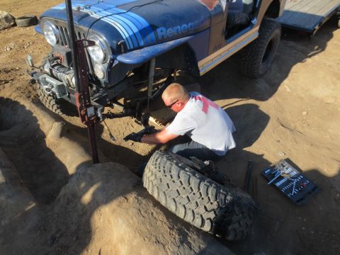 1989 Ford Bronco - A man works on a blue Jeep CJ-7 Renegade, which is on a trailer, with a jack and tools.
