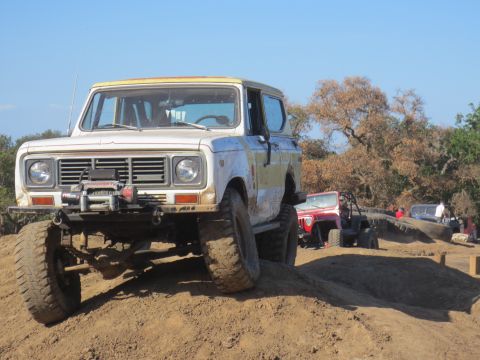 1989 Ford Bronco - Off-road vehicles tackle a dirt course under a clear blue sky.