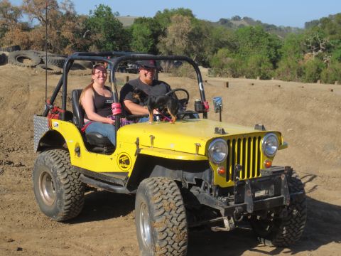 1989 Ford Bronco - Two people and a dog ride in a yellow Jeep CJ-5 on a dirt track.