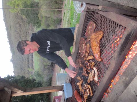 1989 Ford Bronco - A man tends to a large outdoor grill laden with meat cooking over hot coals.