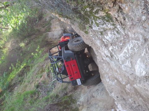 1989 Ford Bronco - A red off-road vehicle is tilted precariously on a steep, rocky trail.