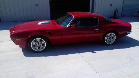 1972 Pontiac Trans Am - A red coupe with a silver hood scoop and unique wheels is parked outside a building.