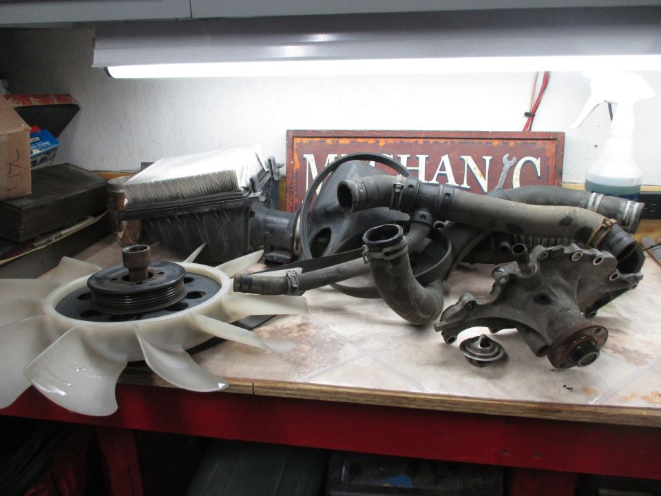 Engine fan, radiator hoses, thermostat, and water pump housing on a workbench