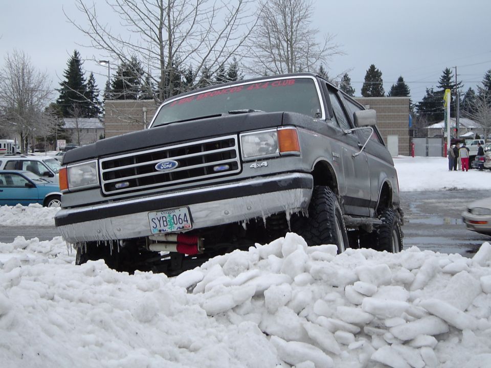 Front of icy two-tone Ford Bronco with SYB-064 plate stuck in snow pile