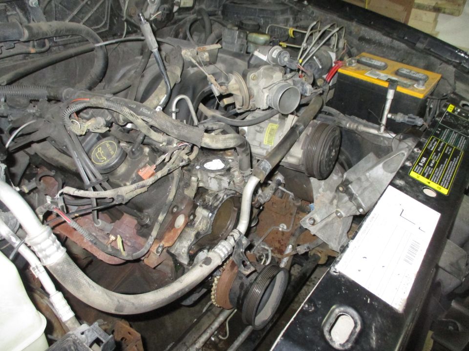 Engine bay with some parts removed, showing the engine block, hoses, and a battery