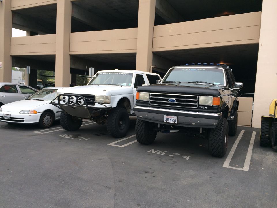 Black Ford truck with custom bumper and white Ford truck with off-road lights parked in a lot