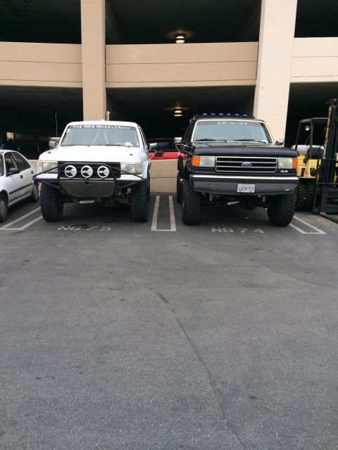 1968 Ford Mustang - Two modified trucks, a white one and a black one, are parked side-by-side in a parking lot.