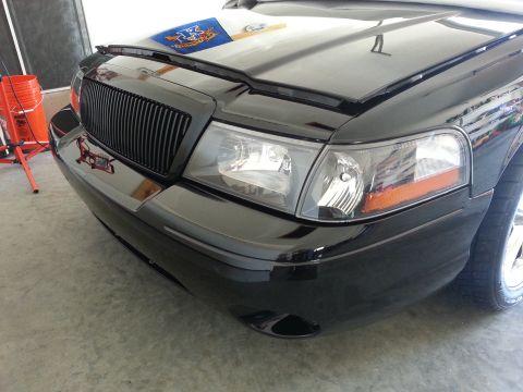 2003 Mercury Marauder - The front end of a black sedan is shown, a custom grille and clear headlights, with the hood partially open.