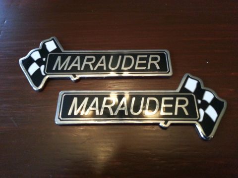 2003 Mercury Marauder - Two Mercury Marauder emblems are displayed on a wooden surface.