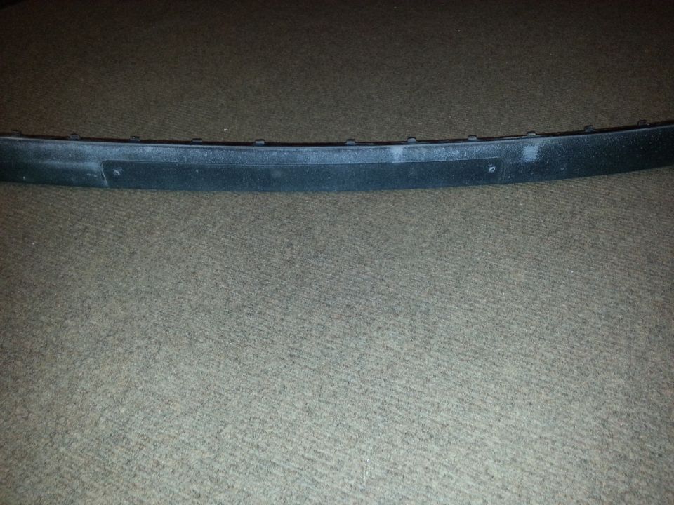 Black plastic trim piece with visible mounting holes, resting on carpet