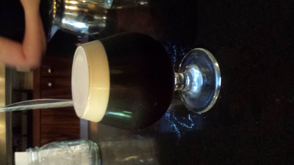 Glass of dark beer with a thick white head, on a dark surface