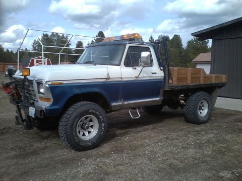 1973 Ford F-250 - This 1973 Ford F-250 flatbed truck is equipped with a plow and warning lights, suggesting utility use.