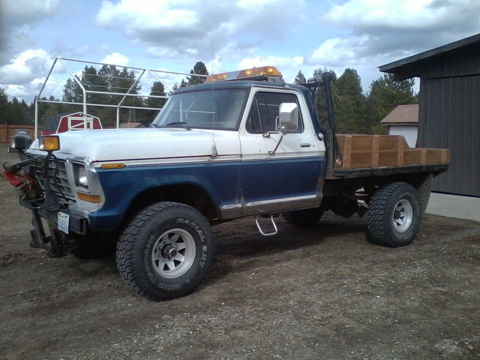 1973 Ford F-250 flatbed truck, white and blue, with a plow attachment and amber warning lights