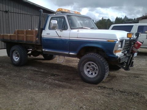 1973 Ford F-250 - This 1973 Ford F-250 features a flatbed with wooden sides and a prominent yellow light bar on the roof.