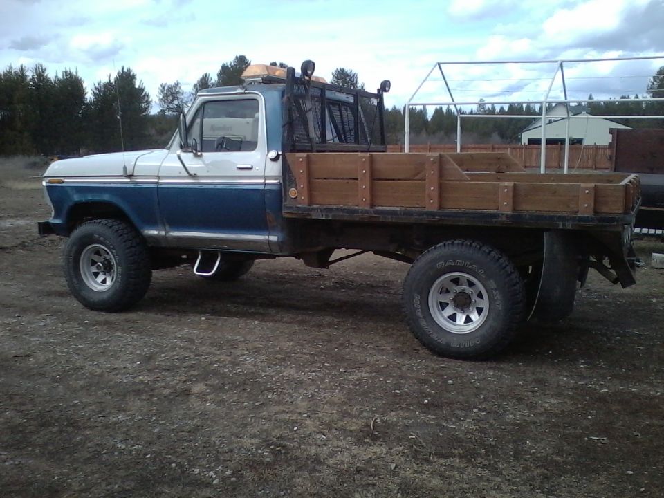 Two-tone blue and white Ford F-Series flatbed truck with wooden bed and rack