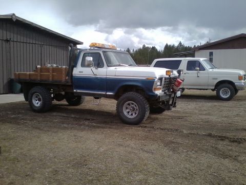 1973 Ford F-250 - A blue and white 1973 Ford F-250 flatbed truck is parked next to a white SUV.