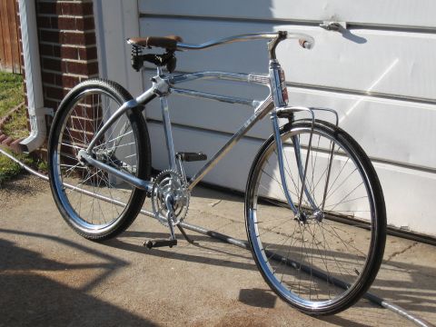 Chrome bicycle with brown seat and black tires, parked on concrete