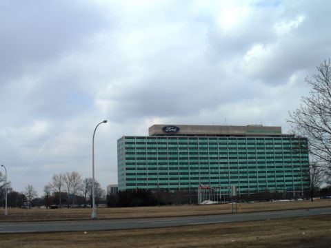 1971 Ford Ranchero - The large Ford Motor Company building stands under a cloudy sky, with a prominent Ford logo visible on its roof.