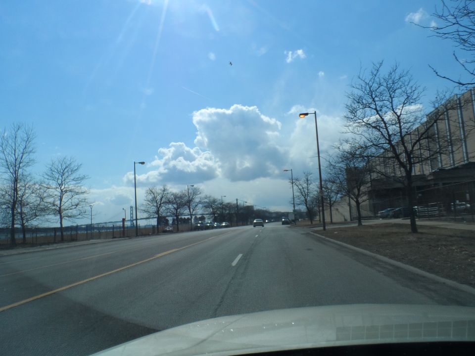 Driving down a road with cars and a large building on the right