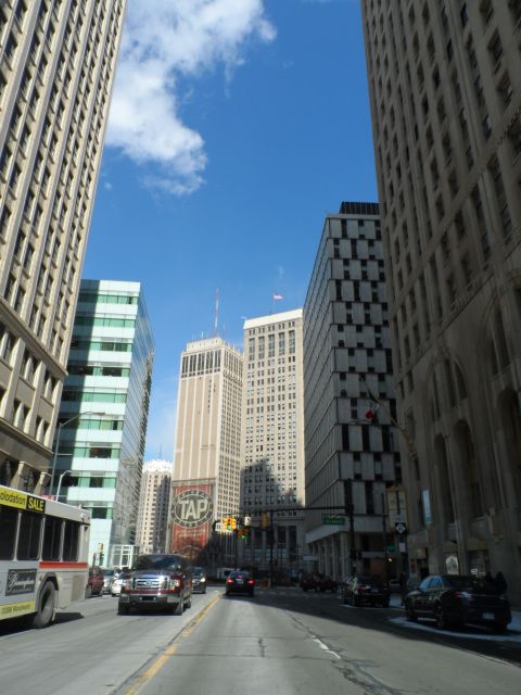 1971 Ford Ranchero - A city street scene unfolds with a bus, a pickup truck, and other vehicles navigating between imposing skyscrapers under a blue sky.