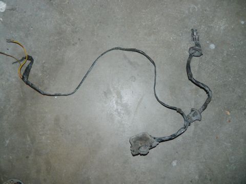 1979 Ford Bronco - A vehicle wiring harness lies on a concrete surface, showing its connectors and protective grommets.